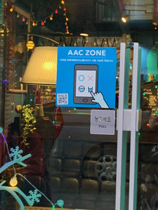 A picture on the front door of the coffee shop in South Korea. On the door is a sticker which indicates that the shop is part of the AAC zone.